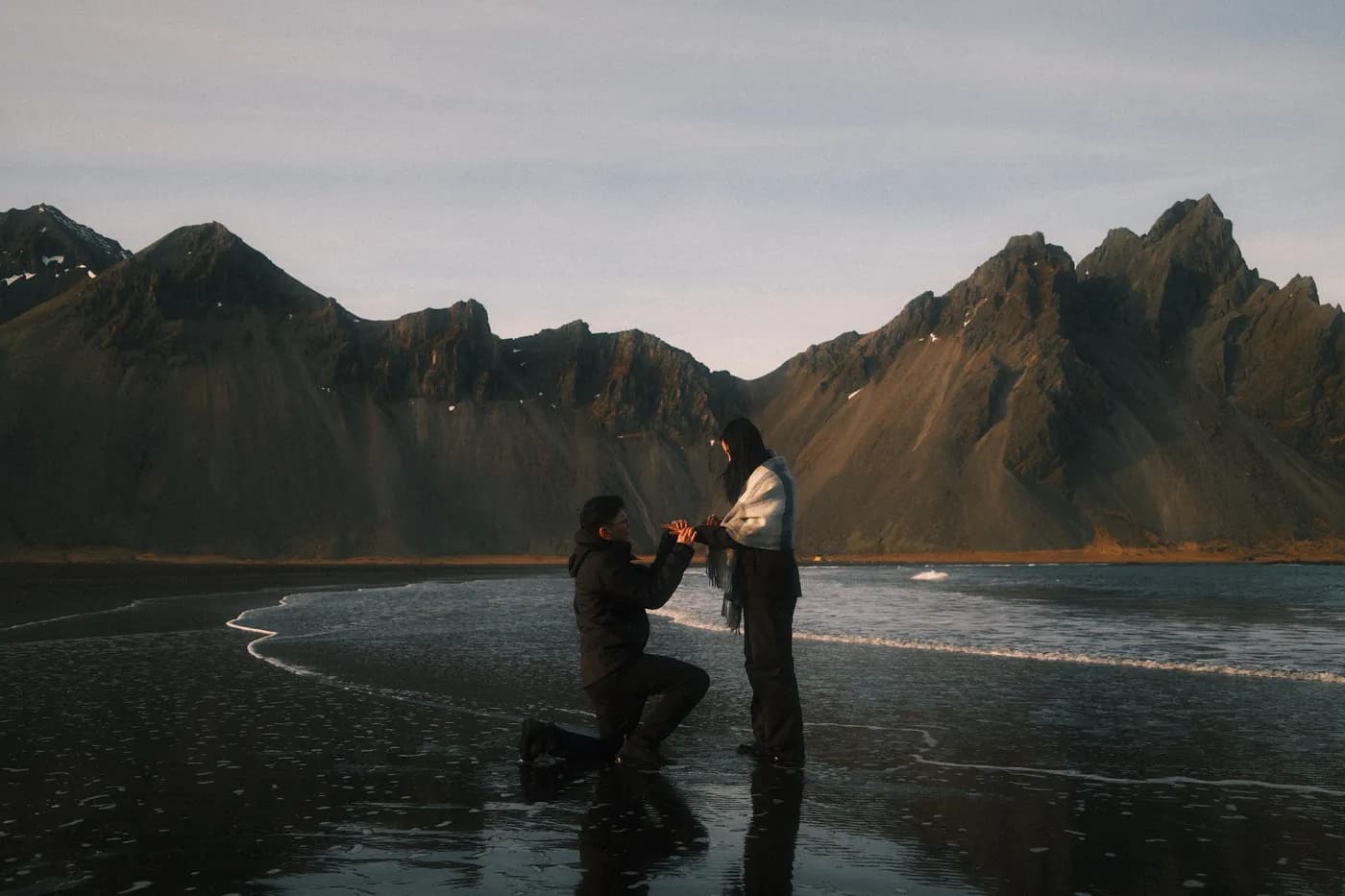 Felix on one knee proposing to Livia on the black sand beach at Stokksnes